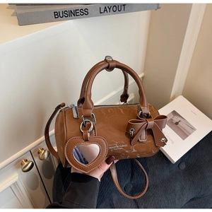 Detail of a brown glossy barrel bag with a 3D bow decoration and heart mirror charm