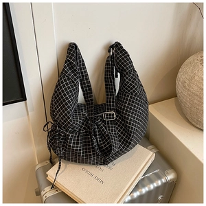 Detail of checkered tote bag with adjustable metal buckle and side drawstring on luggage