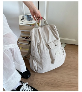Detail of a beige lightweight nylon backpack featuring multiple pockets in a cozy setting