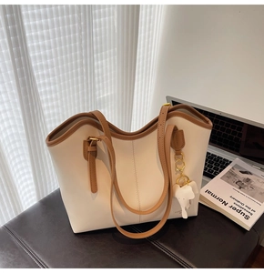 Detail of cream white tote bag with brown straps and cute elephant charm on a desk