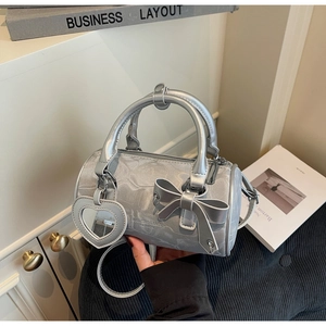 Detail of silver metallic cylinder bag with bow and heart mirror charm on a white background