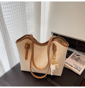 Detail of minimalist cream and tan tote bag with elephant charm in a cozy workspace setting