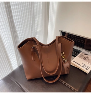 Detailed close-up of brown leather tote bag with vertical stitching and elephant charm