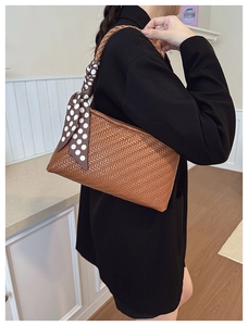 Close-up of brown woven shoulder bag with chic polka dot scarf detail on black blazer
