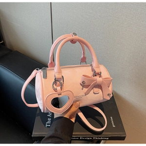 Pink cylinder handbag featuring stylish bow decoration and heart-shaped mirror charm
