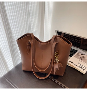 Brown tote bag detail with elephant charm shown next to a laptop in office setting