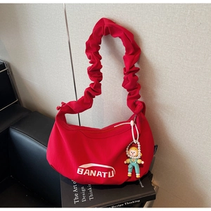 Détail du sac croissant rouge en toile avec bandoulière plissée et pendentif poupée