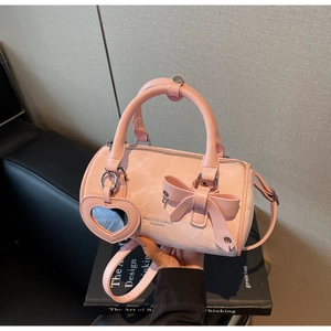 Detail of pink cylindrical handbag with a decorative bow and heart-shaped mirror charm