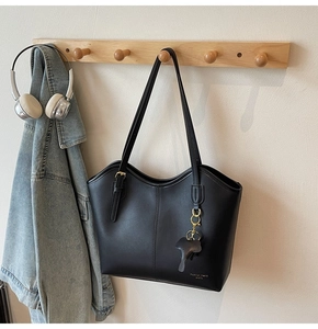 Detail of minimalist black leather tote bag featuring an elephant charm and brand text