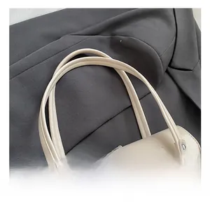 Detail einer cremefarbenen Handtasche mit Metallverschluss und stabilen Doppelgriffen