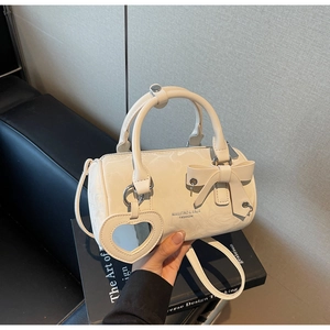 Detail of cream cylinder bucket bag with bow accent and heart mirror charm accessory