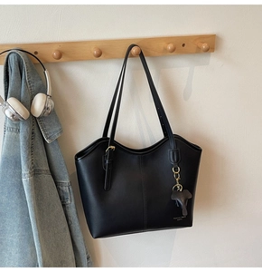 Detail of a minimalist black tote bag with gray elephant charm on a wooden hook