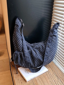 Blue plaid half-moon crossbody bag with drawstring detail on a wooden table surface