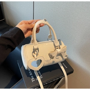 Detail of cream cylindrical handbag featuring a bow accent and heart mirror charm