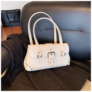Detail der cremeweißen Schultertasche mit Silbernieten und Metallschnalle auf Ledersofa