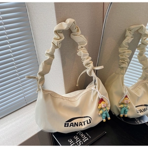Vue détaillée du sac beige plissé en toile avec breloque poupée et reflet dans le miroir