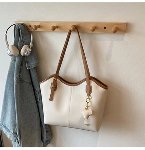 Detail view of cream tote bag with brown trim and cute elephant charm on a wooden hook