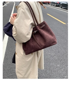 Detail of suede tote bag with leather side straps and silver metal buckles shown on model