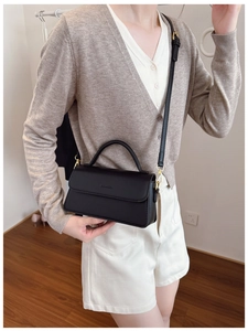 Detail of black rectangular bag with gold metal buckles and adjustable leather shoulder strap