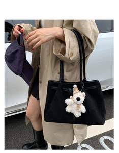 Close-up of black suede tote bag featuring a cute teddy bear pendant and textured surface