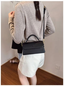 Detail of minimalist black leather crossbody bag with subtle logo and adjustable strap