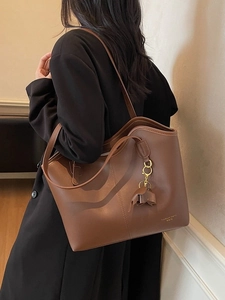 Minimalist brown leather tote bag with tassel charm and sleek vertical stitching details