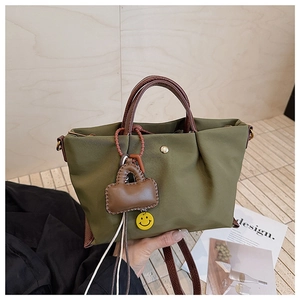 Détail du sac à main vert armée en toile avec anses en cuir marron et breloque souriante