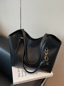Minimalist black faux leather tote bag with vertical stitching and golden hardware charm