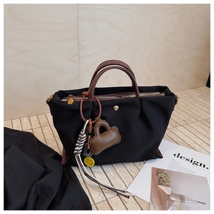 Détail du sac à main noir en toile avec poignées en cuir marron et breloques de mode