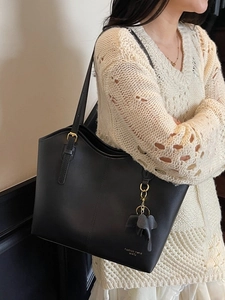 Minimalist black tote bag with elephant charm and gold hardware worn by model