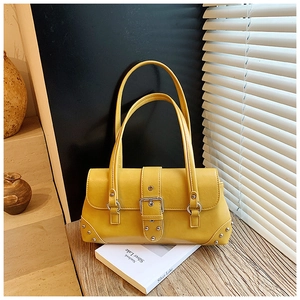 Detailansicht der leuchtend gelben Ledertasche mit Metallschnallen auf einem Holztisch