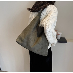 Detail of dark green suede hobo bag worn by a model in a minimalist winter outfit