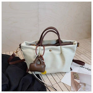 Détail du sac à main en toile plissée crème avec anses en cuir marron et breloque déco