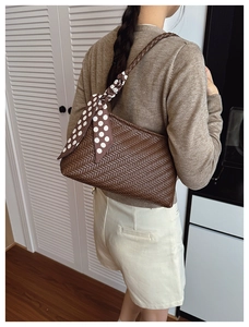 Detail of dark brown woven shoulder bag with elegant white polka dot silk scarf handle decor