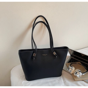 Detail of black faux leather tote bag with white stitching and branded logo on the front