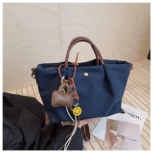 Détail du fourre-tout en nylon bleu marine avec anses en cuir brun et breloque smiley
