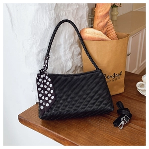 Detail of black woven shoulder bag with chic polka dot scarf on a wooden table
