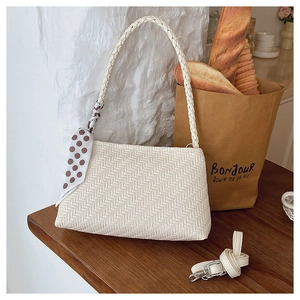 Detail of cream woven underarm bag with decorative polka dot scarf and wooden base