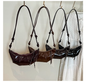 Detail view of high-gloss patent leather croissant bags in four colors hanging on a white wall