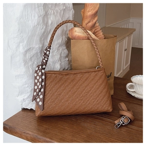 Detailed texture of brown woven shoulder bag featuring silk scarf and adjustable strap