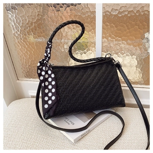 Detailed view of black woven shoulder bag with chic polka dot scarf on a white surface