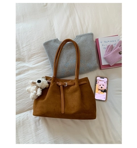 Flat lay of brown suede tote bag with a plush bear charm on soft white bedding