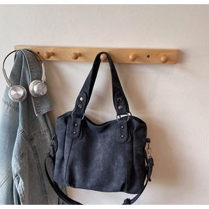 Détail d'un sac cabas vintage gris foncé à texture délavée suspendu à un crochet en bois