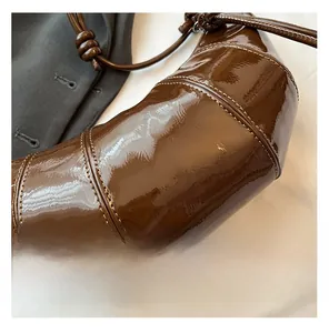 Close-up of brown patent leather crescent bag featuring detailed stitching and knotted strap