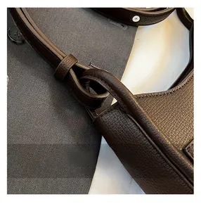 Macro detail of dark brown litchi grain leather bag strap showing fine stitching and oil edge