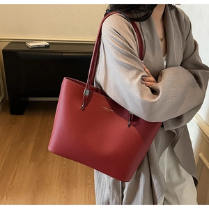 Close-up of red leather tote bag showing fine lychee grain texture and gold brand logo