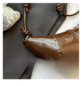 Close-up of knotted shoulder strap on dark brown patent leather croissant bag