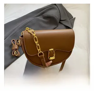Brown saddle bag with gold U-shaped metal buckle and chain handle in a lifestyle setting