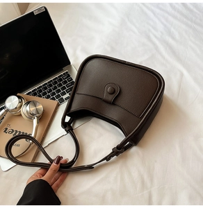 Detail of dark brown lychee leather shoulder bag with buckle on a white bed