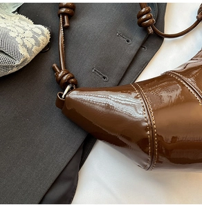 Detailed close-up of dark brown patent leather croissant bag with stylish knot design
